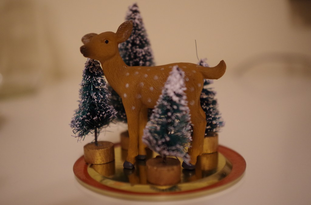 Arrange your festive stuff on the Mason jar's lid. This is important so that you can make sure your festive stuff will actually fit inside of the Mason jar. It's also important to make sure your festive stuff is festive enough. Here, I've created a scene in which the deer is frolicking in a bottle brush tree forest. Frolicking? Definitely festive. Other suggestions for festive snow globe items include snowmen, non-terrifying Santa Claus figurines (if you can find one), tiny recreations of Dickensian town squares, velociraptors covered in Christmas lights, velociraptors covered in Christmas lights attacking tiny recreations of Dickensian town squares, and tiny replicas of your enemies wearing only their undergarments so that they'll be forever trapped in a freezing, watery, festive globe of terror. 